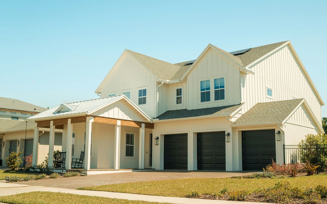 A brand-new two-story white farmhouse-style home with a front porch and three-car garage in Lake Nona, Florida